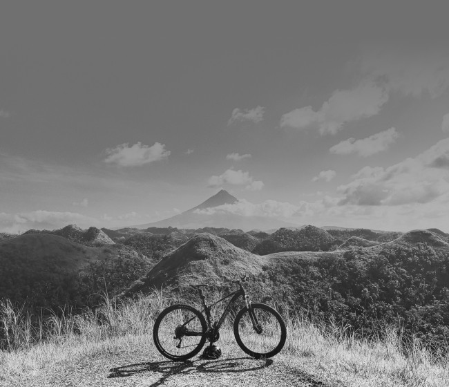 A bicycle parked on a hilltop overlooking rolling hills with a volcanic peak in the distance.